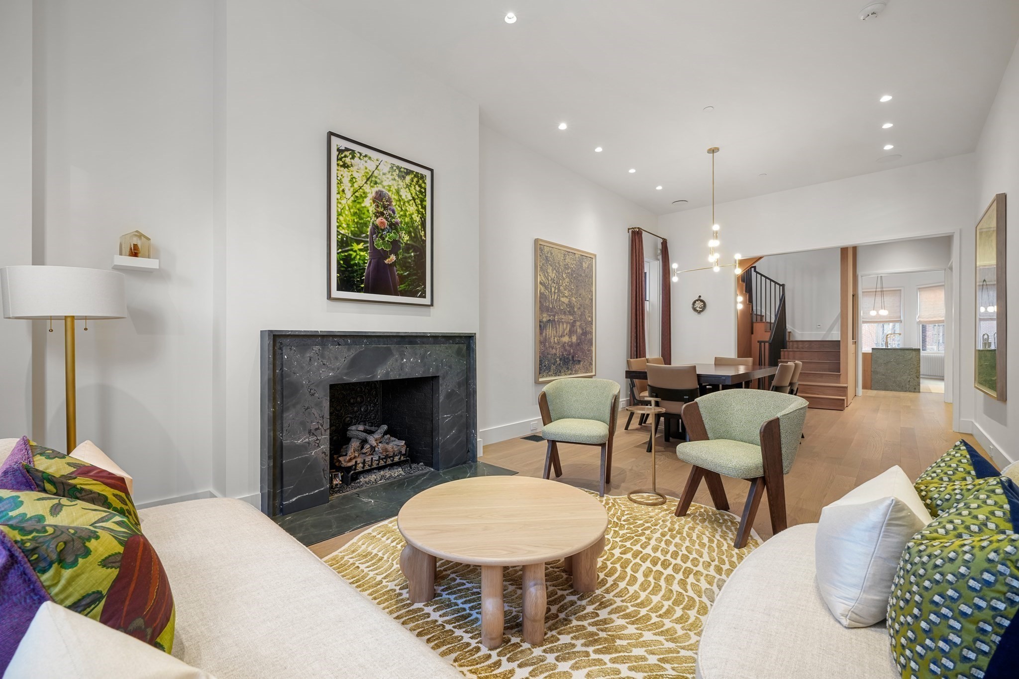 Living and dining room with a stone fireplace, patterned rug, and staircase.