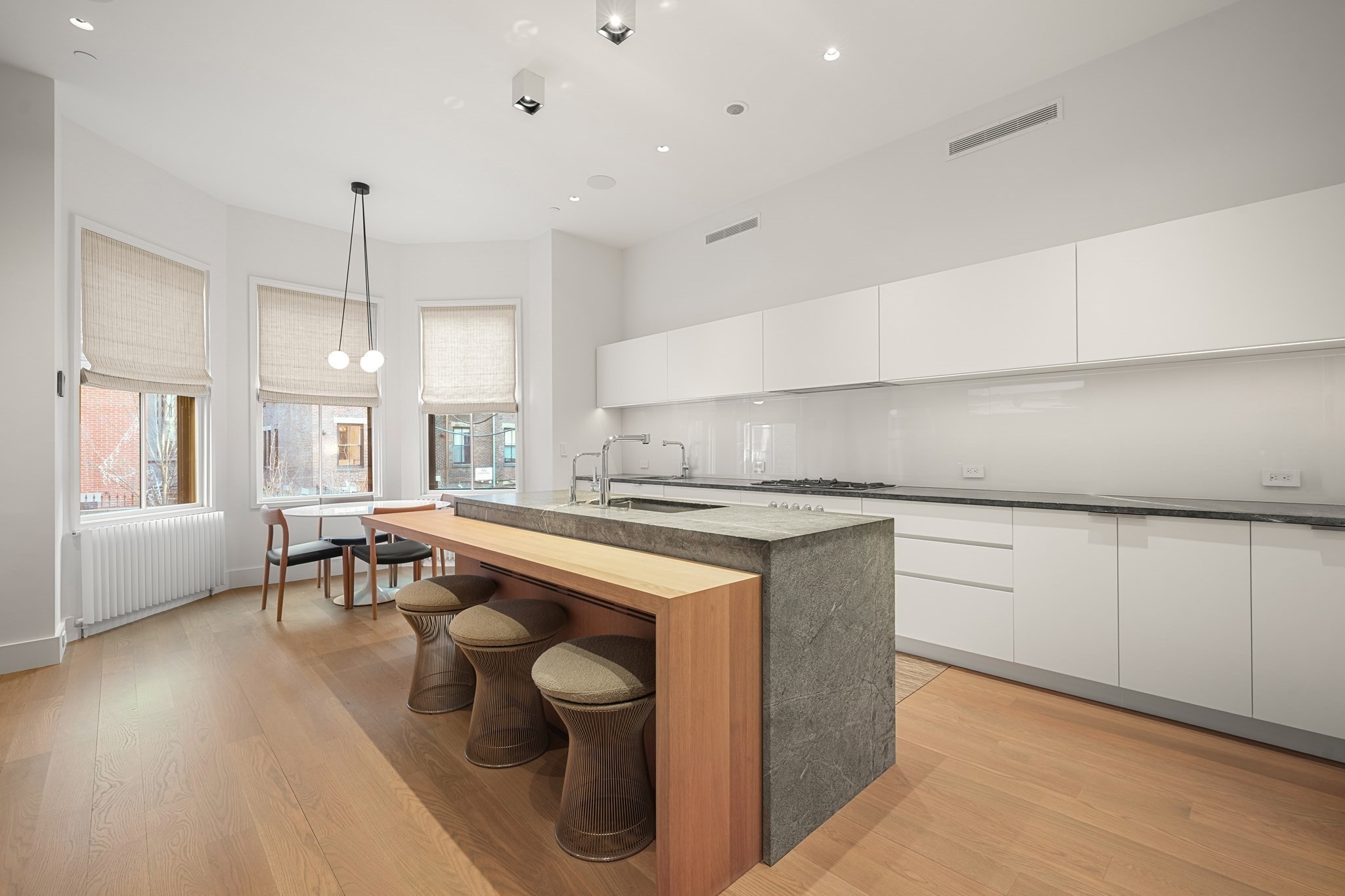 Modern kitchen with a gray stone island, wood breakfast bar, and three tall windows.