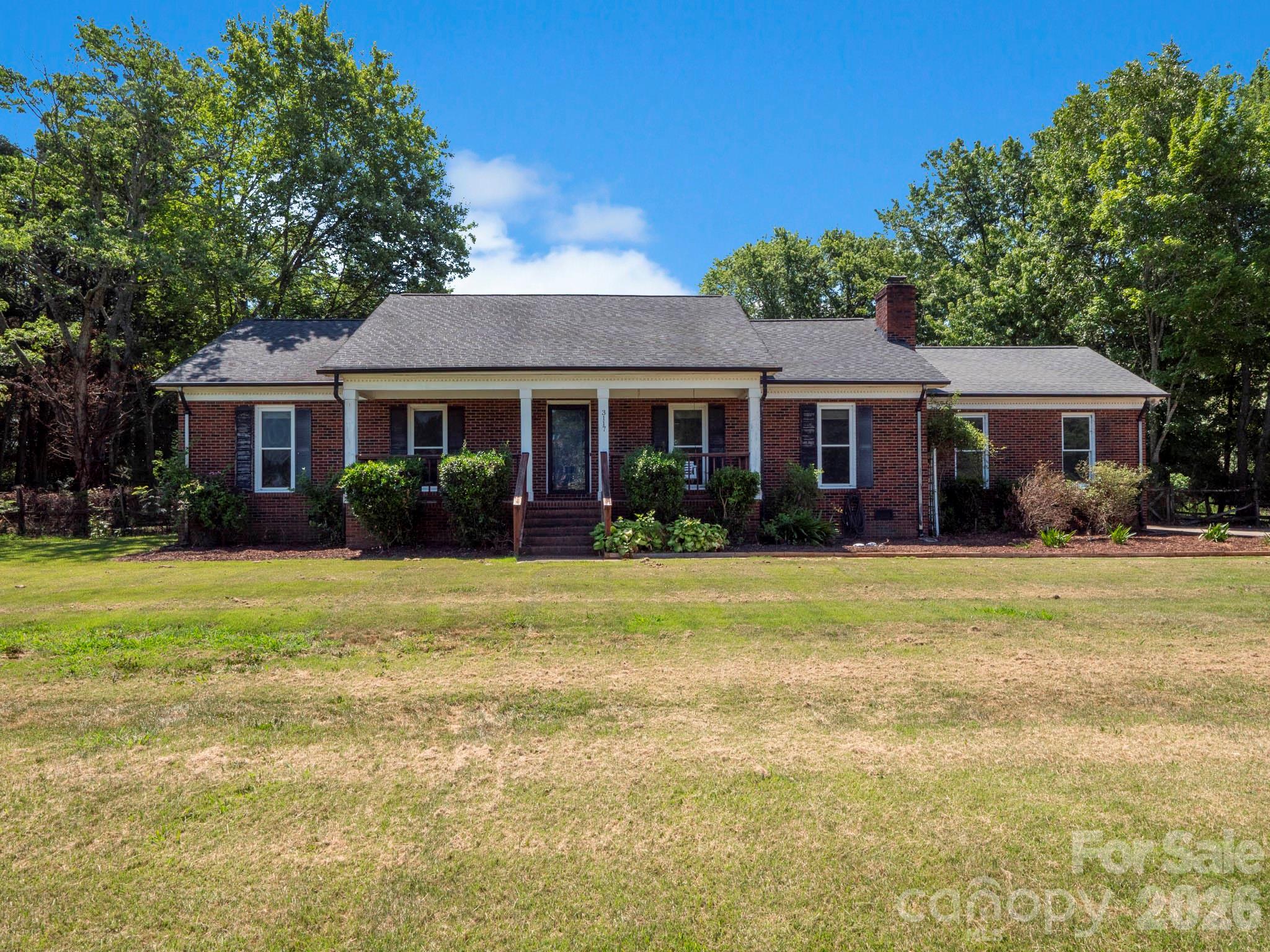 Red-brick ranch home with a covered front porch, broad lawn, and mature trees.