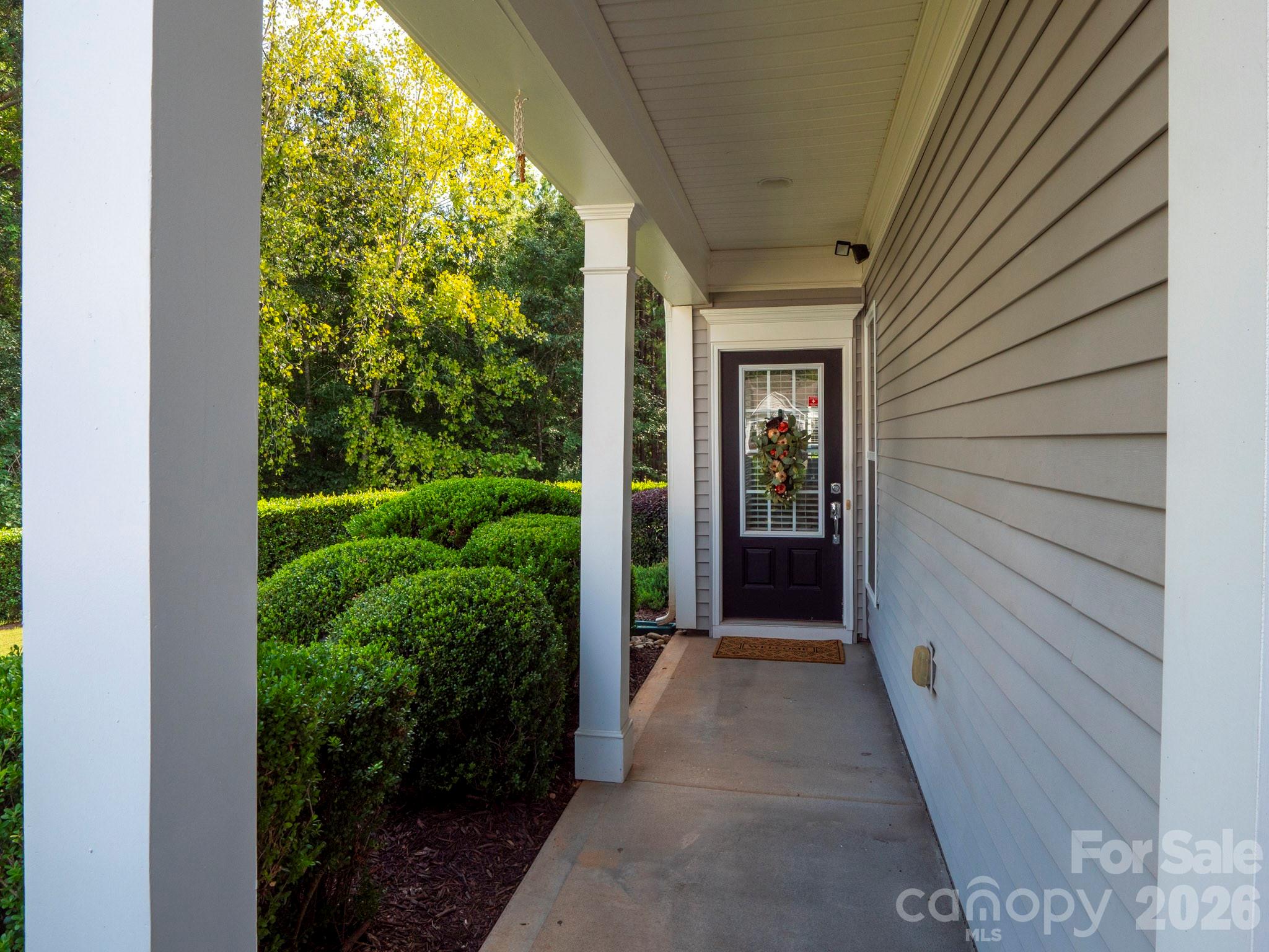 Covered front porch with white columns, a wreath on the dark entry door, and trimmed shrubs.