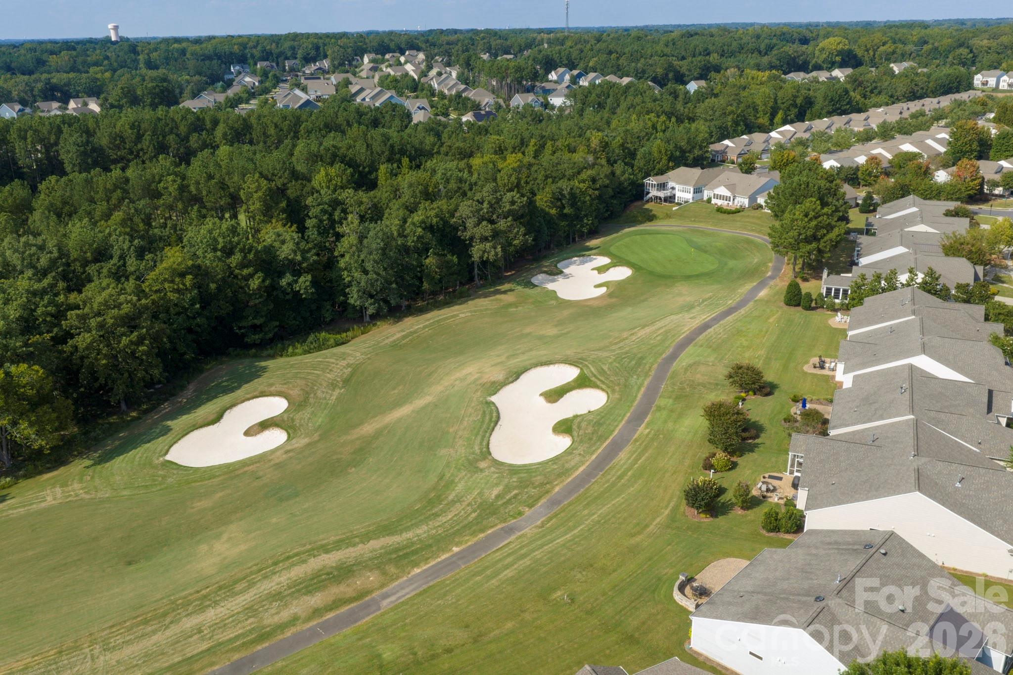 Aerial golf course with white sand bunkers, a winding cart path, trees, and homes along one side.