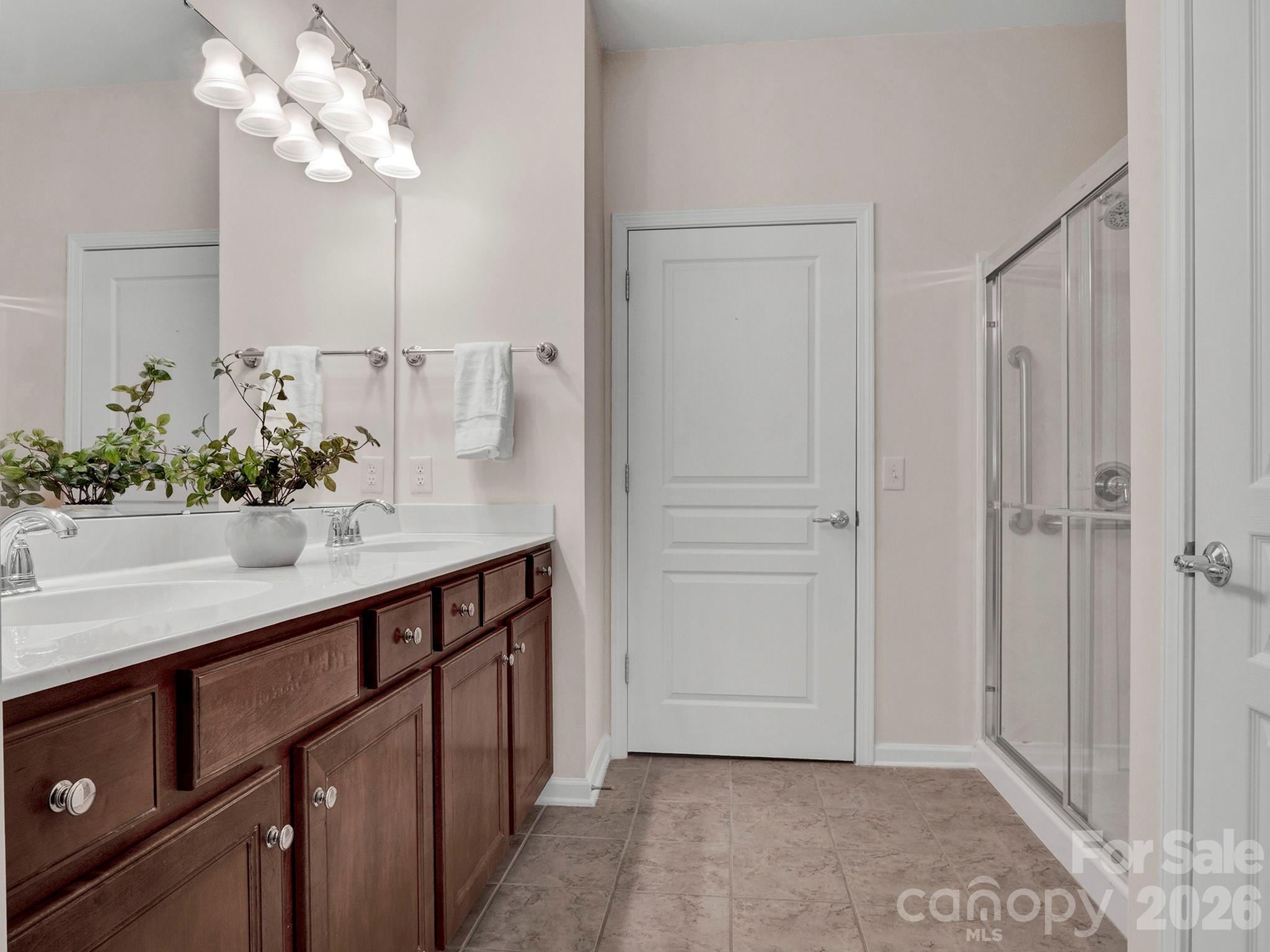 Bathroom with a dark wood double vanity, mirrored wall, and glass-enclosed shower.