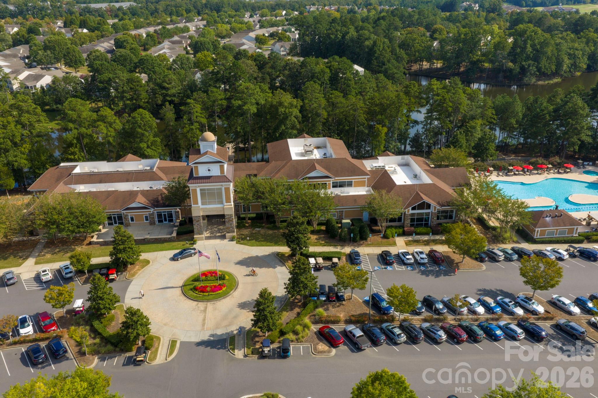 Community clubhouse and pool beside a wooded lake, viewed from above.