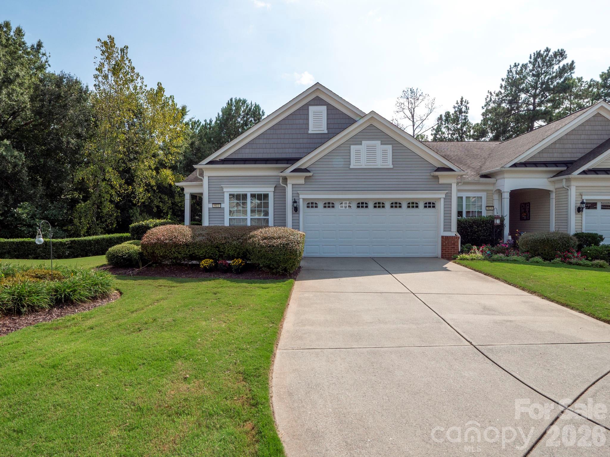 Gray home with white trim, a two-car garage, wide driveway, and landscaped front yard.