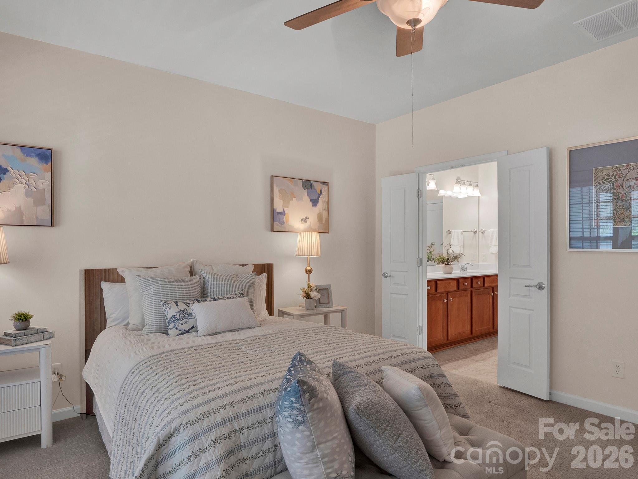 Staged bedroom with patterned white bedding and an open view into an ensuite bathroom.
