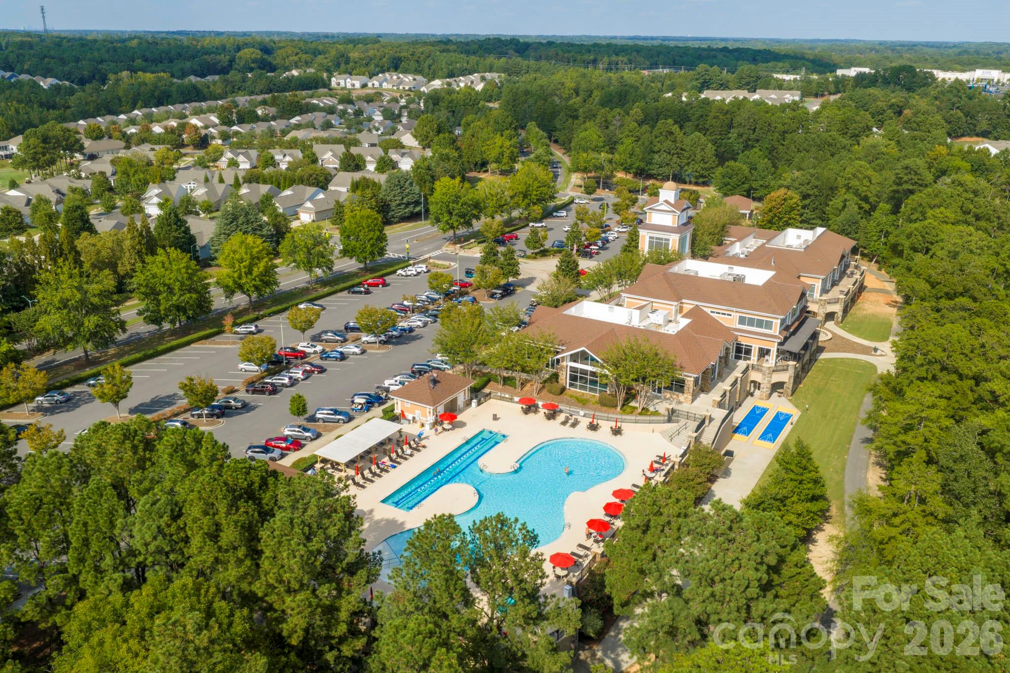 Aerial view of a community clubhouse, swimming pool, parking lot, and surrounding homes.