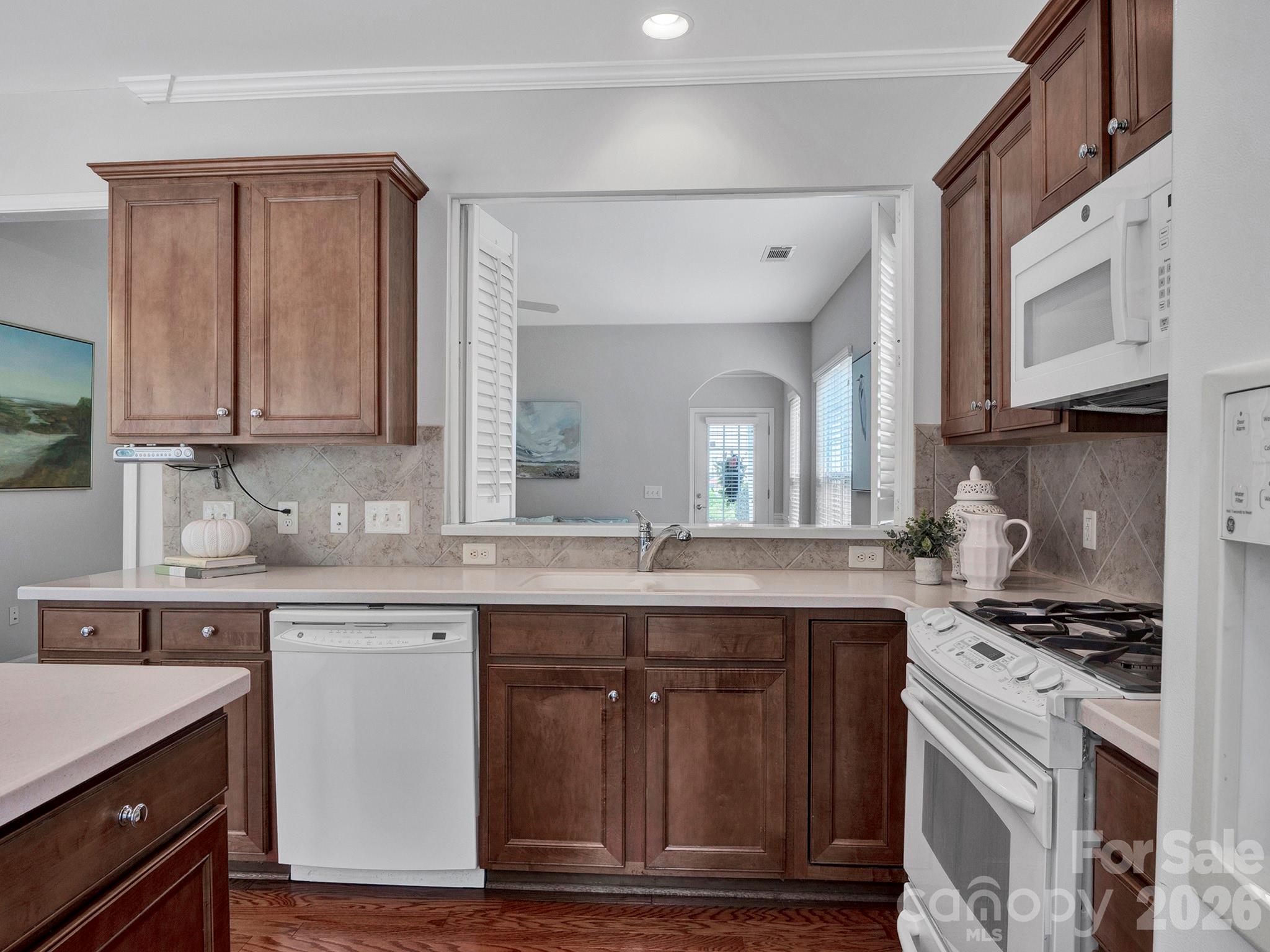 Kitchen with dark wood cabinets, a tile backsplash, white dishwasher, and range.