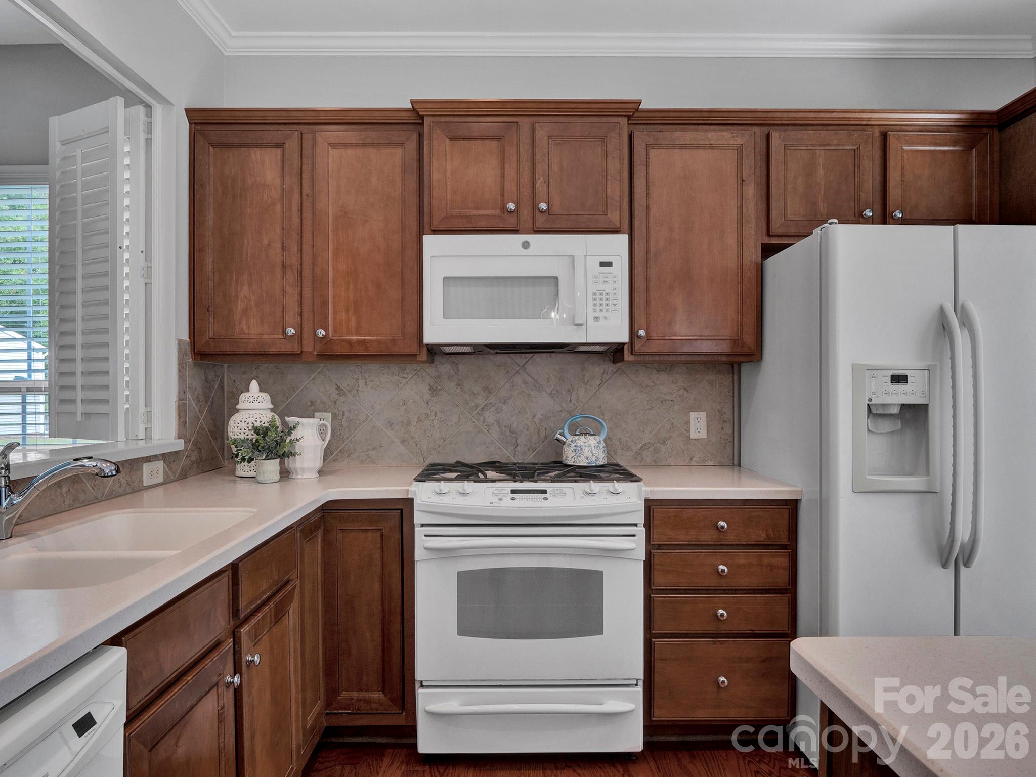 Kitchen with dark wood cabinets, white appliances, pale counters, and a diagonal tile backsplash.
