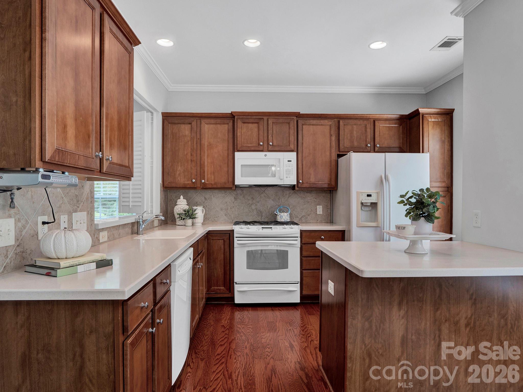 Kitchen with rich wood cabinets, white appliances, light countertops, and hardwood floors.