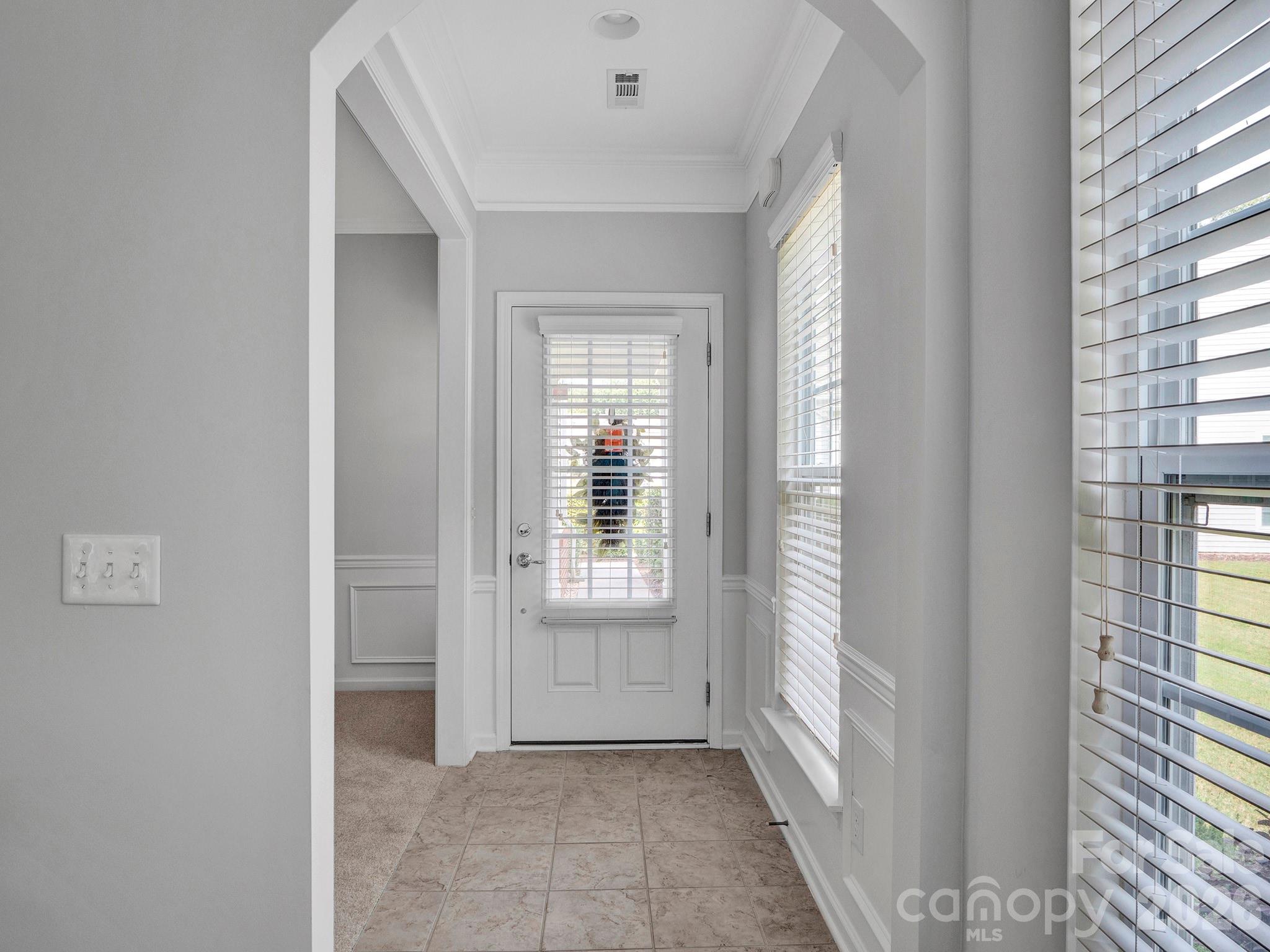 Entryway with tiled floor, white blind-covered front door, and large windows.