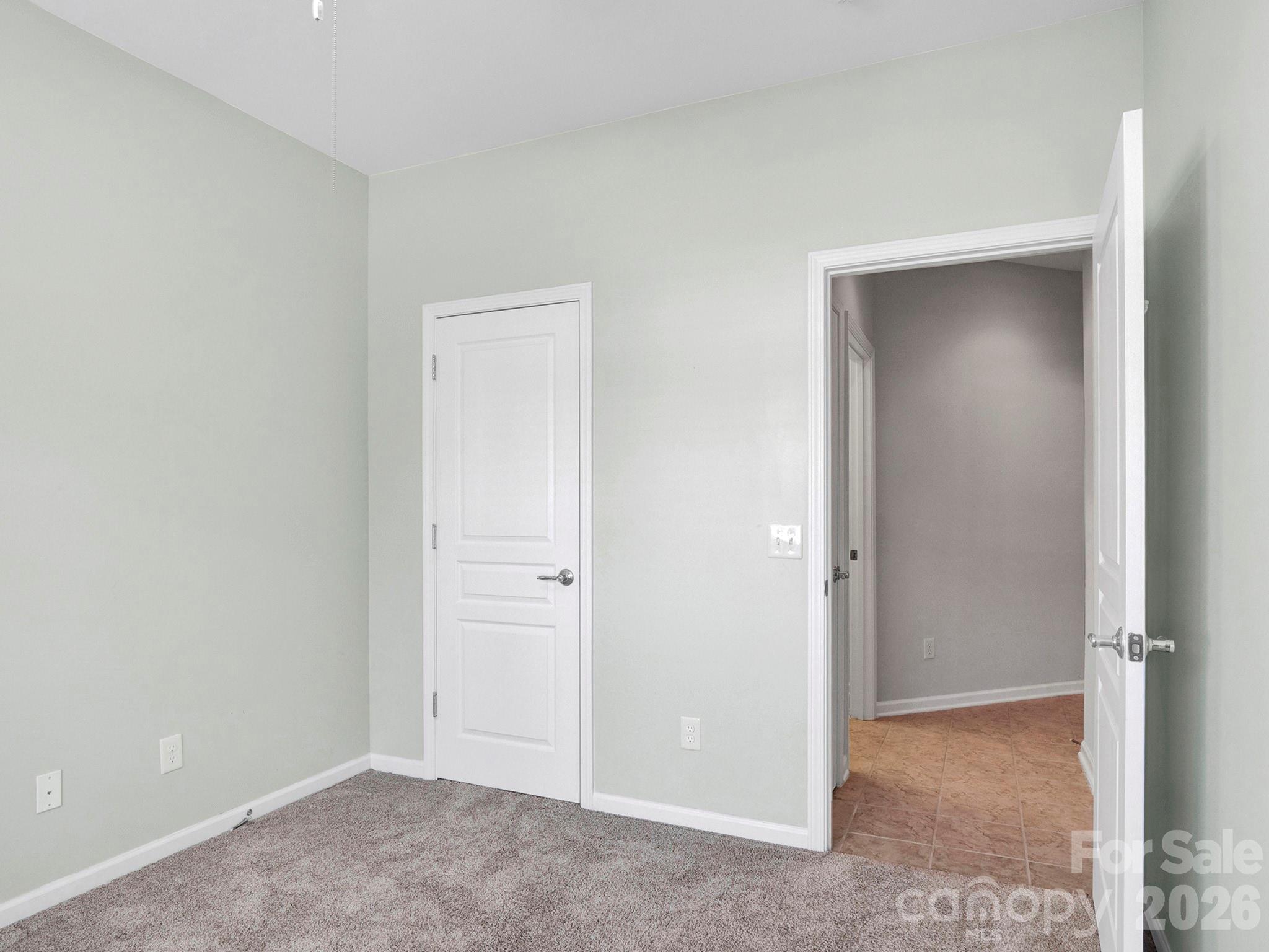 Empty carpeted room with pale walls and an open doorway to a tiled area.
