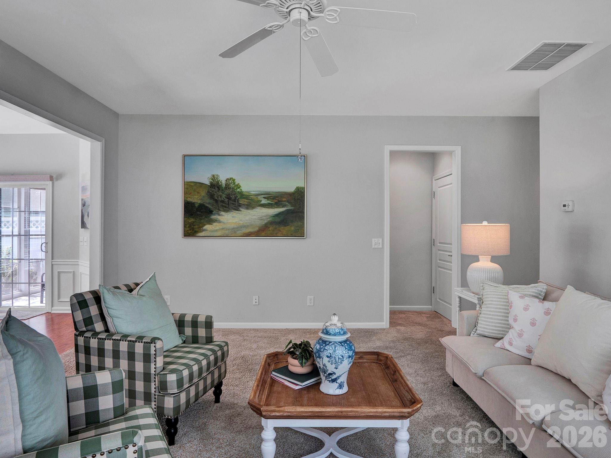 Furnished living room with a plaid armchair, light sofa, and wooden coffee table.