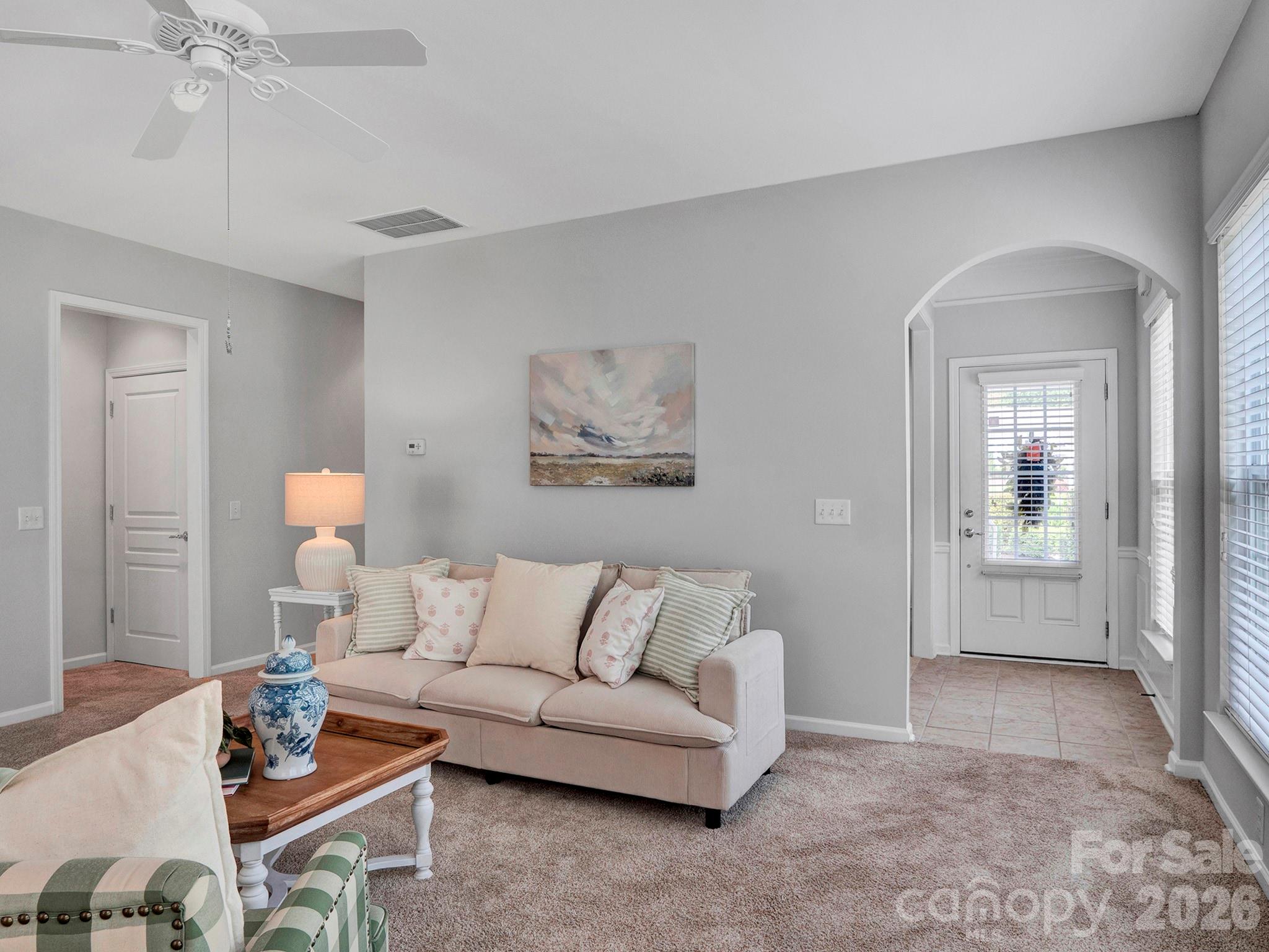 Furnished living room with a beige sofa, blue-and-white vase, and arched entryway.
