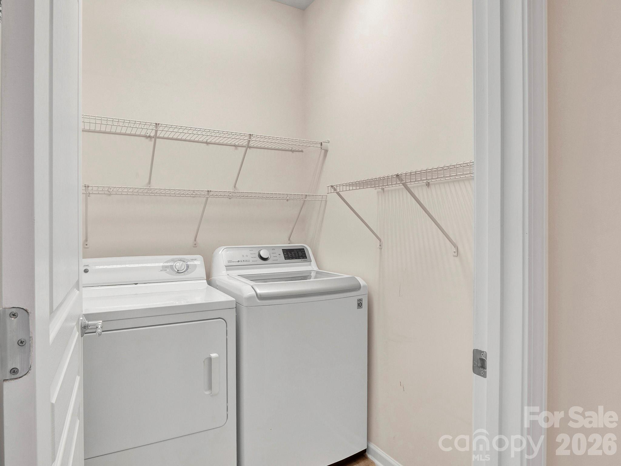 Laundry room with a white washer and dryer beneath wall-mounted wire shelving.