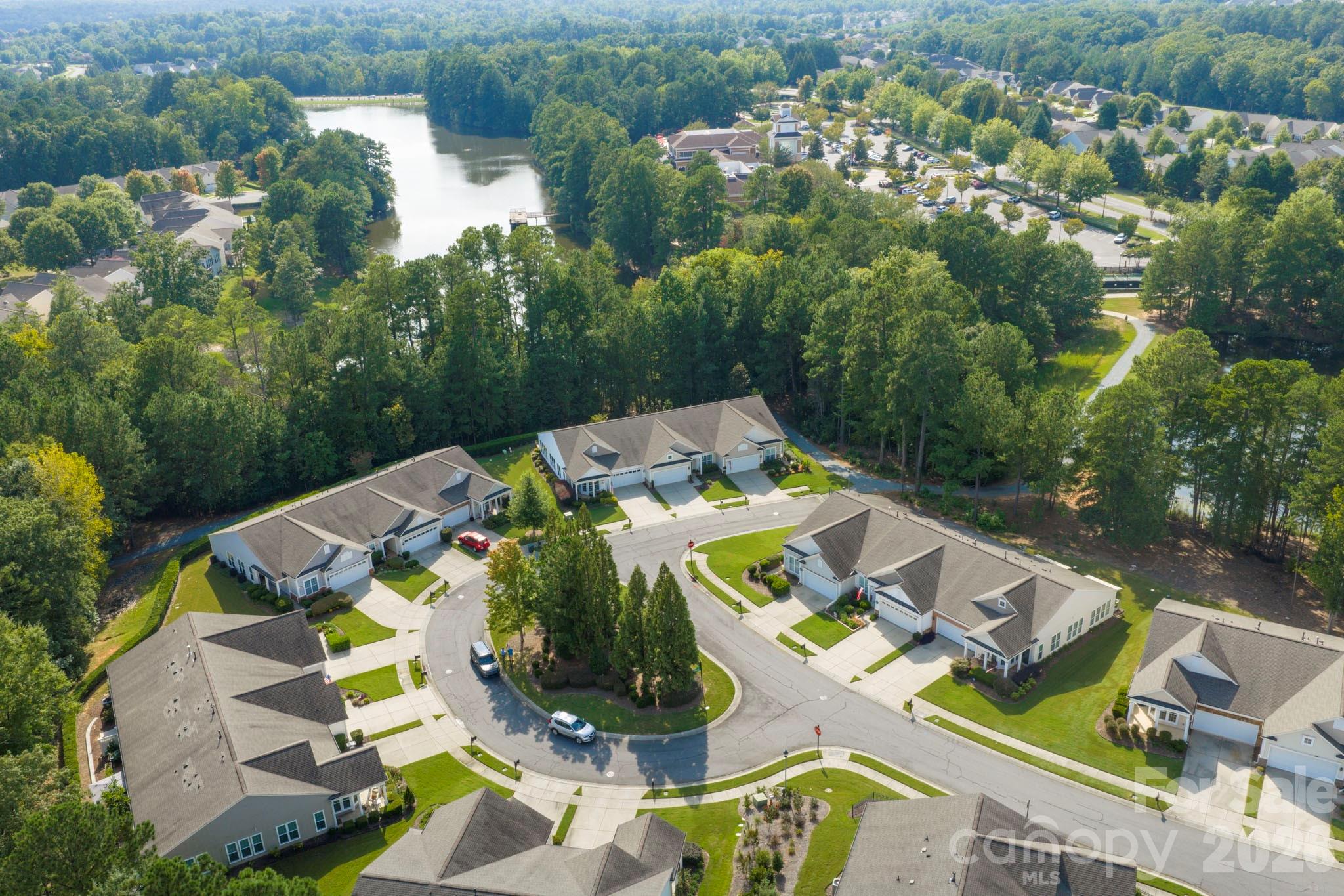 Aerial view of homes around a cul-de-sac, with wooded surroundings and a lake nearby.