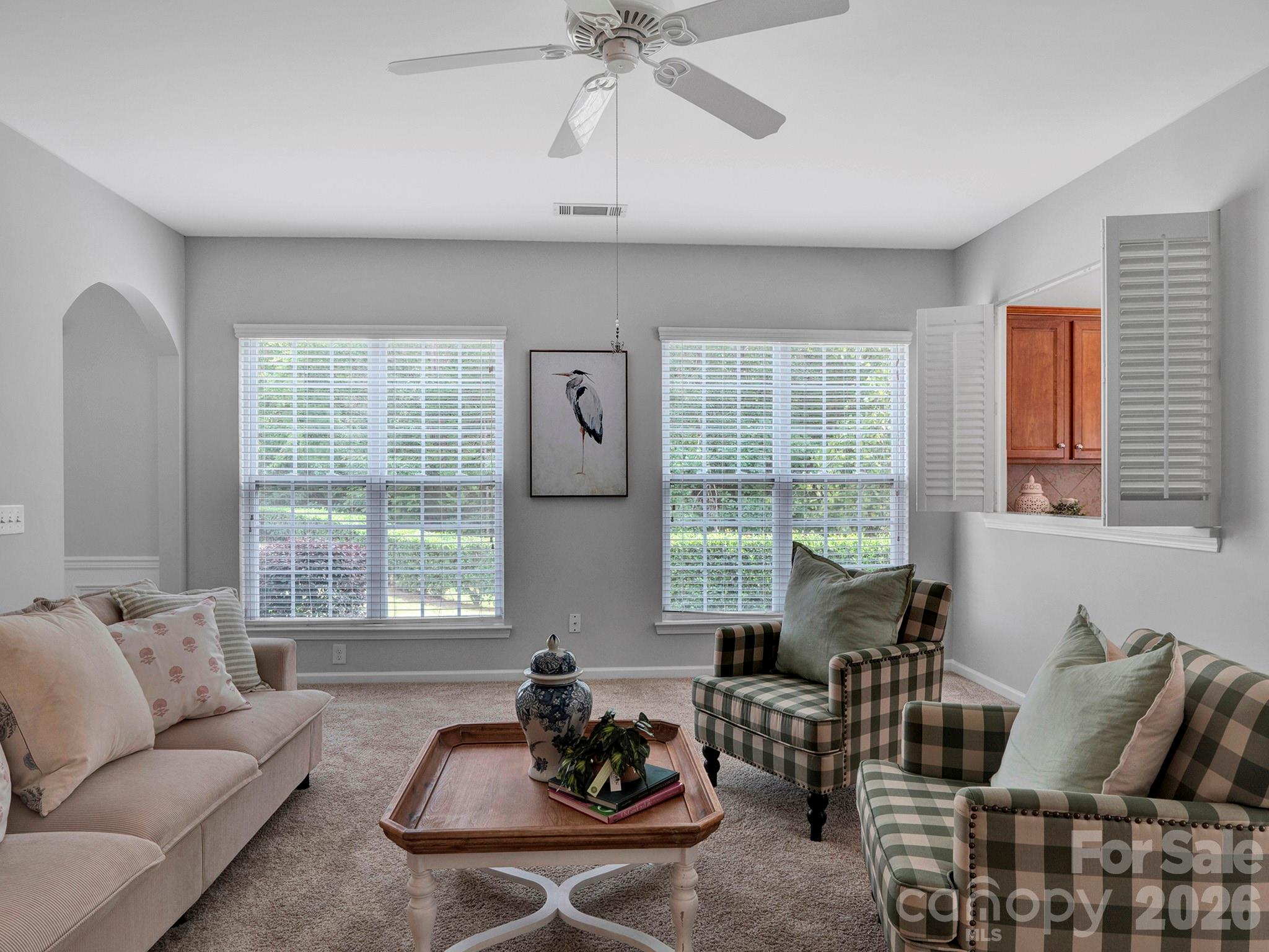Living room with plaid armchairs, a cream sofa, and two wide windows overlooking greenery.