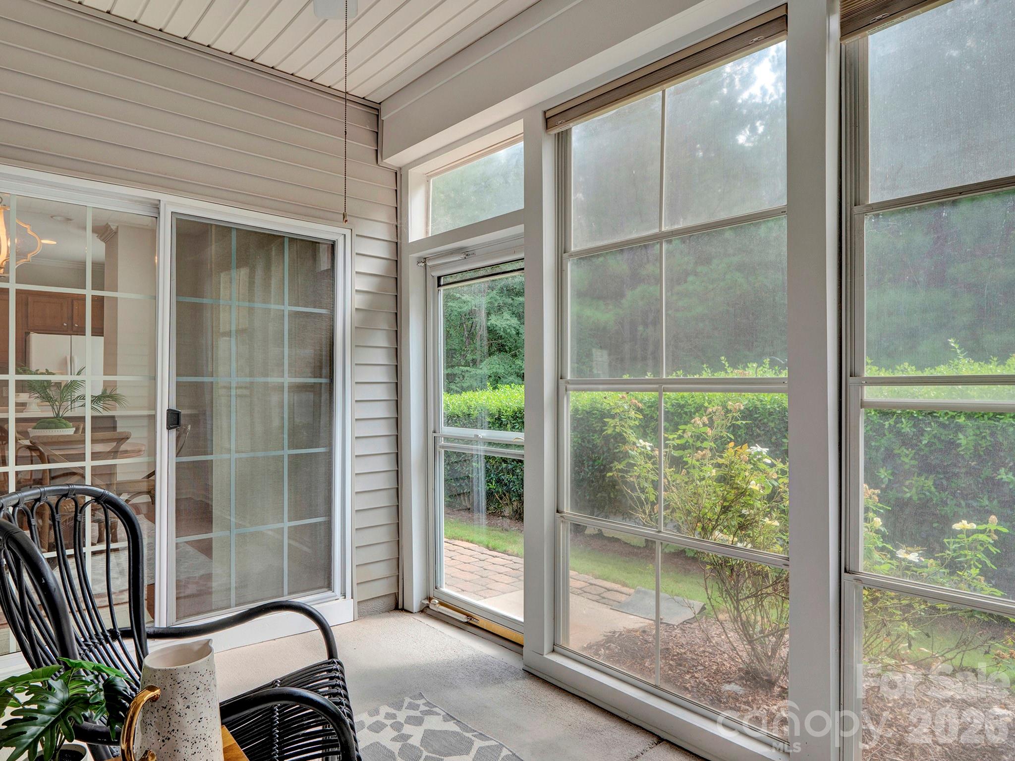 Furnished sunroom with tall windows overlooking a landscaped garden.