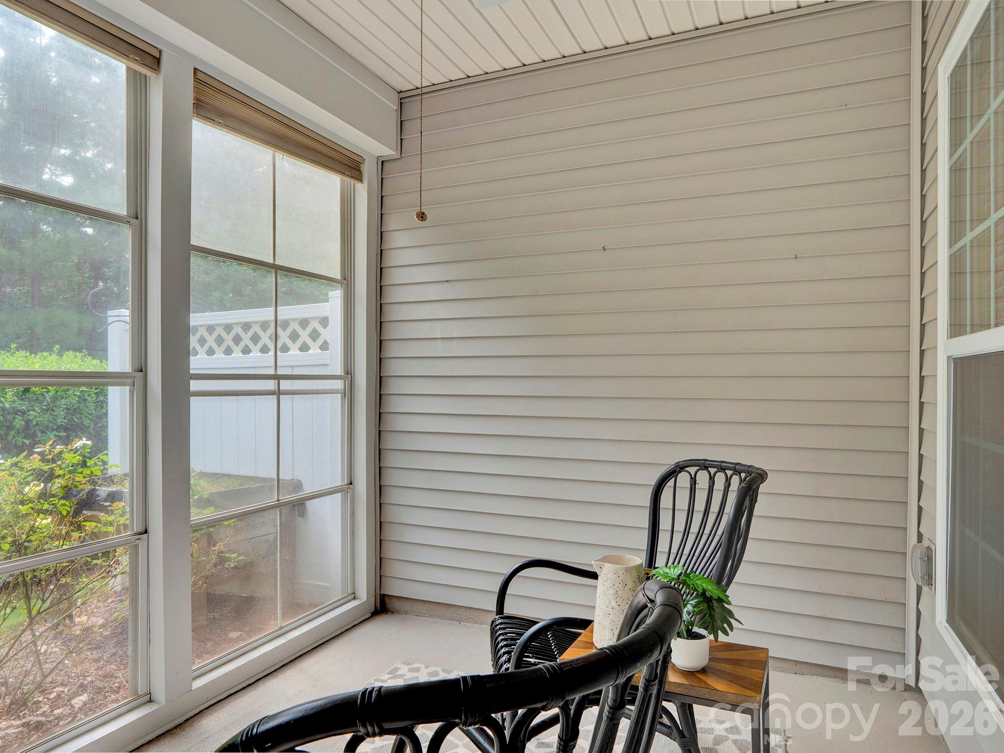 Enclosed porch with large windows, black wicker chairs, and a small table with a potted plant.