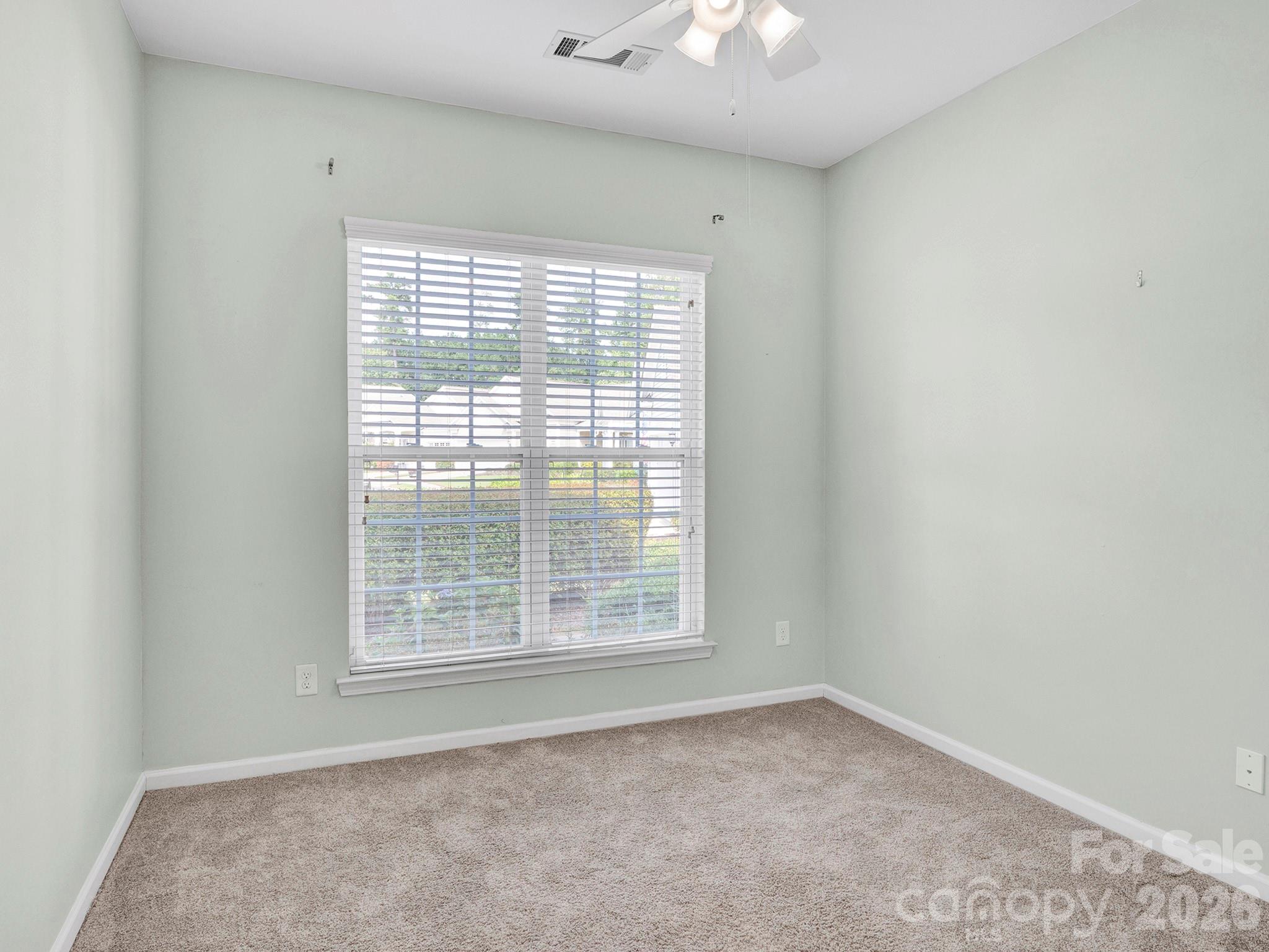 Empty bedroom with beige carpet, pale green walls, and a large window with white blinds.