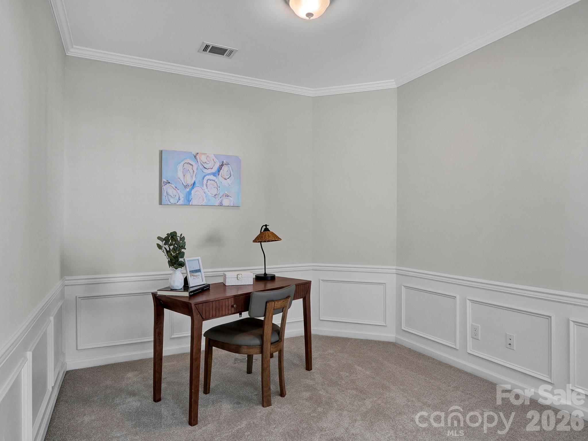Furnished home office with a dark wood desk and chair, paneled walls, and floral artwork.