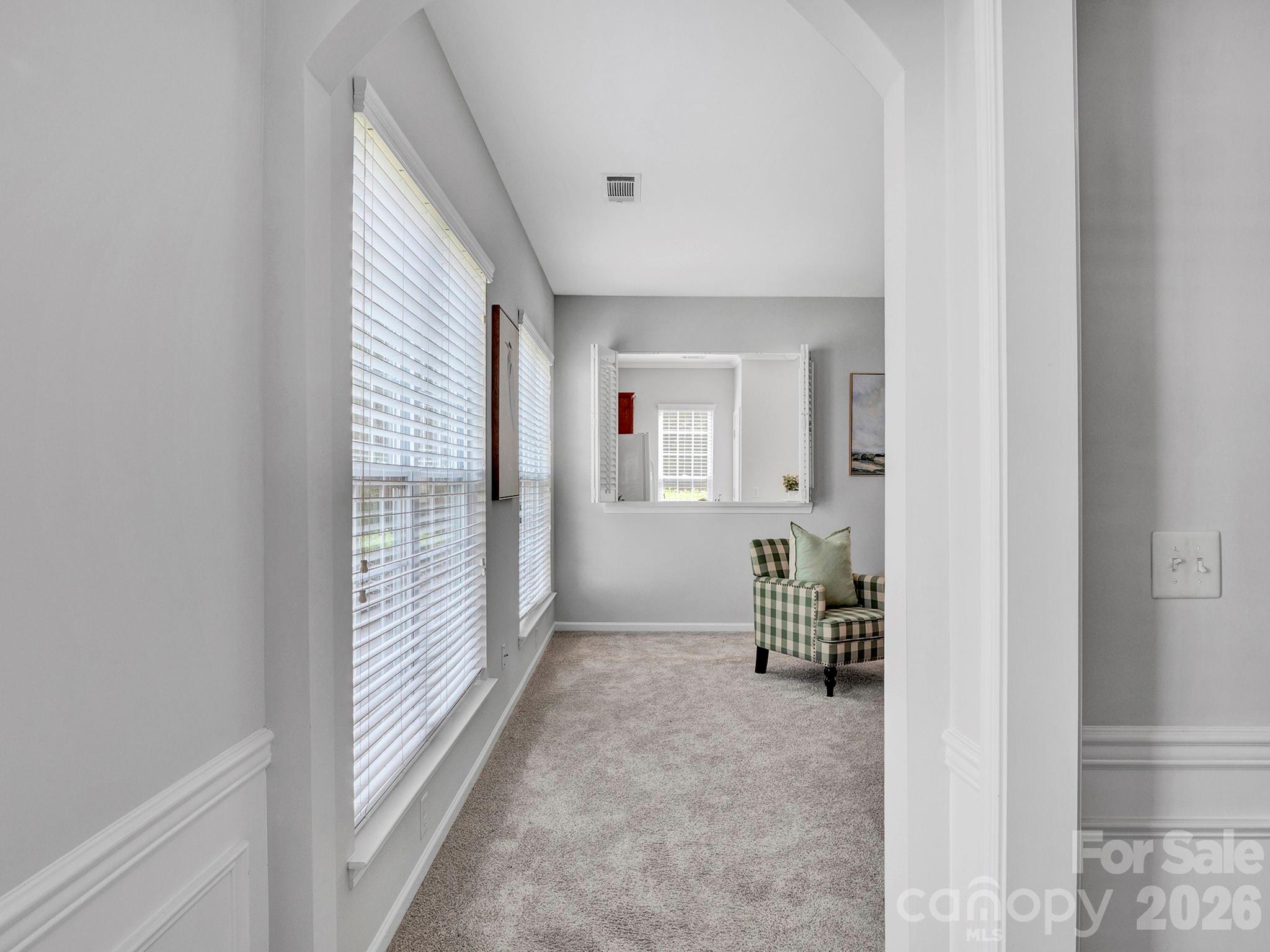Sitting room with a vaulted ceiling, tall blinded windows, and a green checkered armchair.