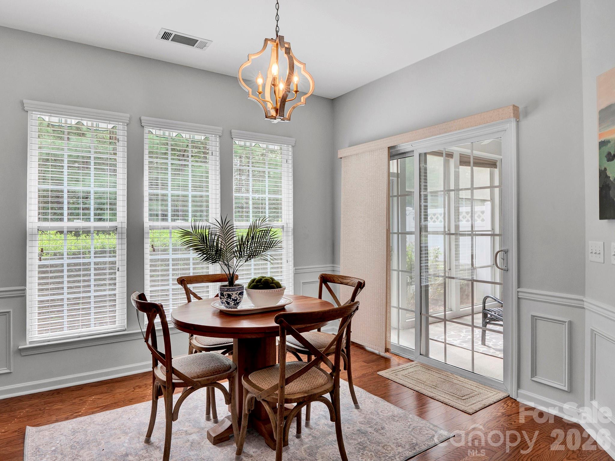 Dining room with a round wooden table, four chairs, three bright windows, and a glass-paneled patio door.