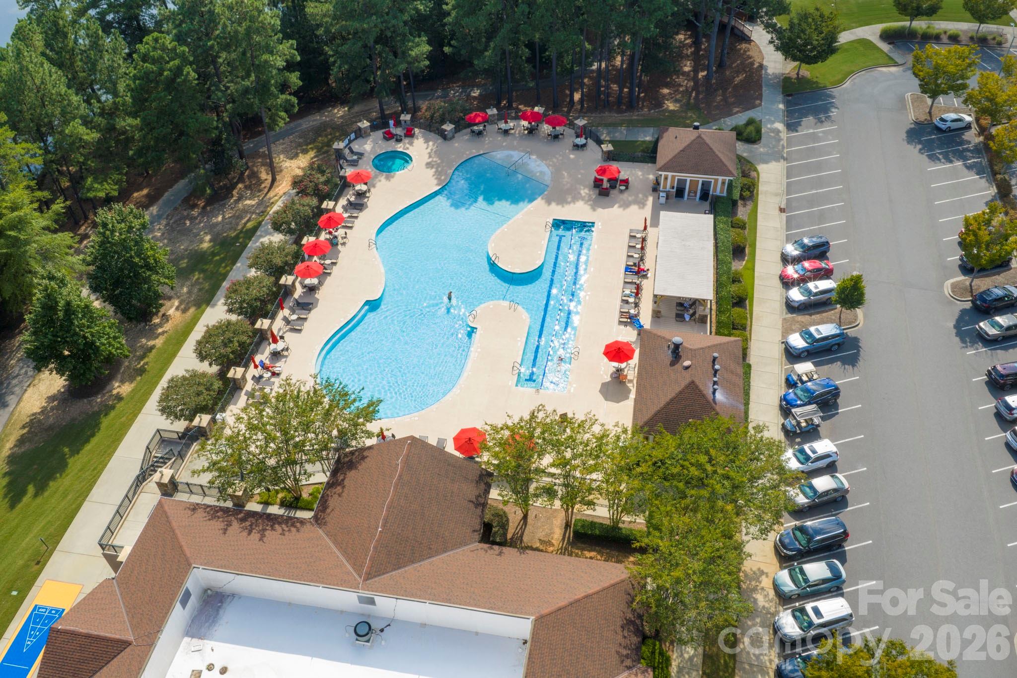 Community pool with a separate lap lane, red umbrellas, and surrounding trees, seen from above.