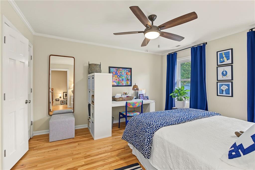 Bedroom with blue curtains, patterned bedding, hardwood floors, and a ceiling fan.