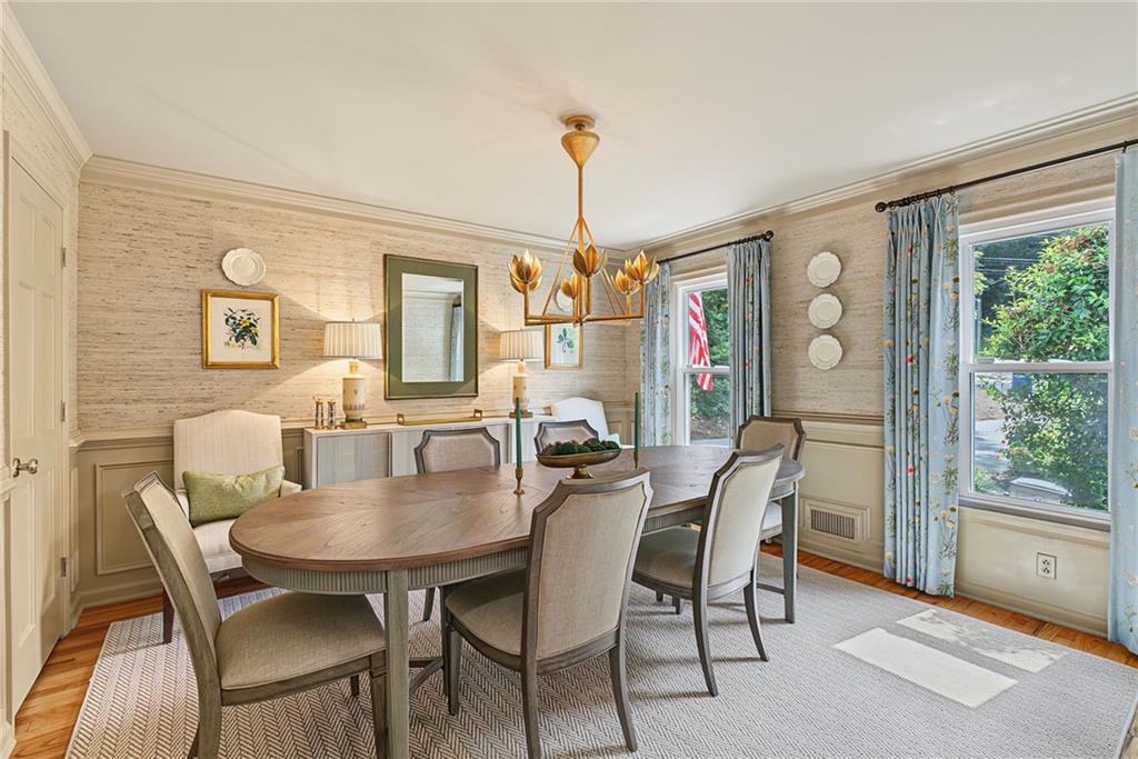 Dining room with an oval table, upholstered chairs, gold chandelier, and blue floral curtains.