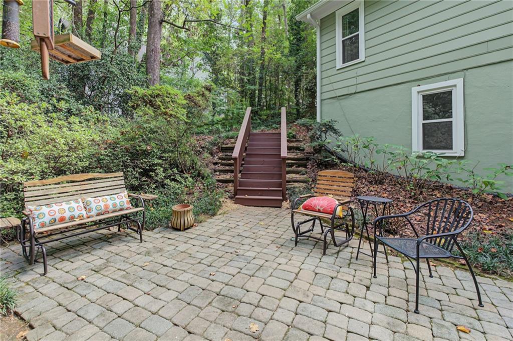 Stone patio with outdoor seating and steps leading into a wooded garden beside the house.