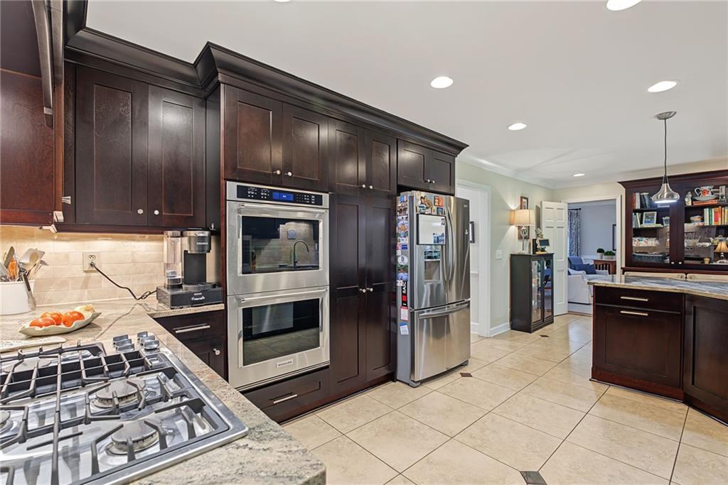 Kitchen with dark wood cabinets, granite counters, stainless steel appliances, and beige tile flooring.
