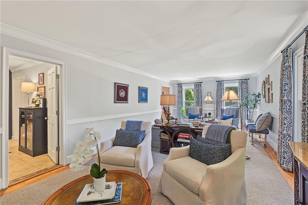 Furnished living room with cream armchairs, a round coffee table, and tall patterned curtains.