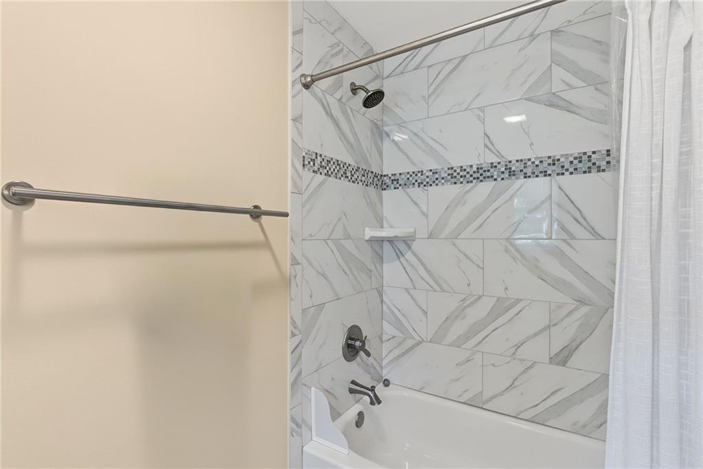 Bathroom tub and shower with marble-look tile and a gray mosaic accent strip.