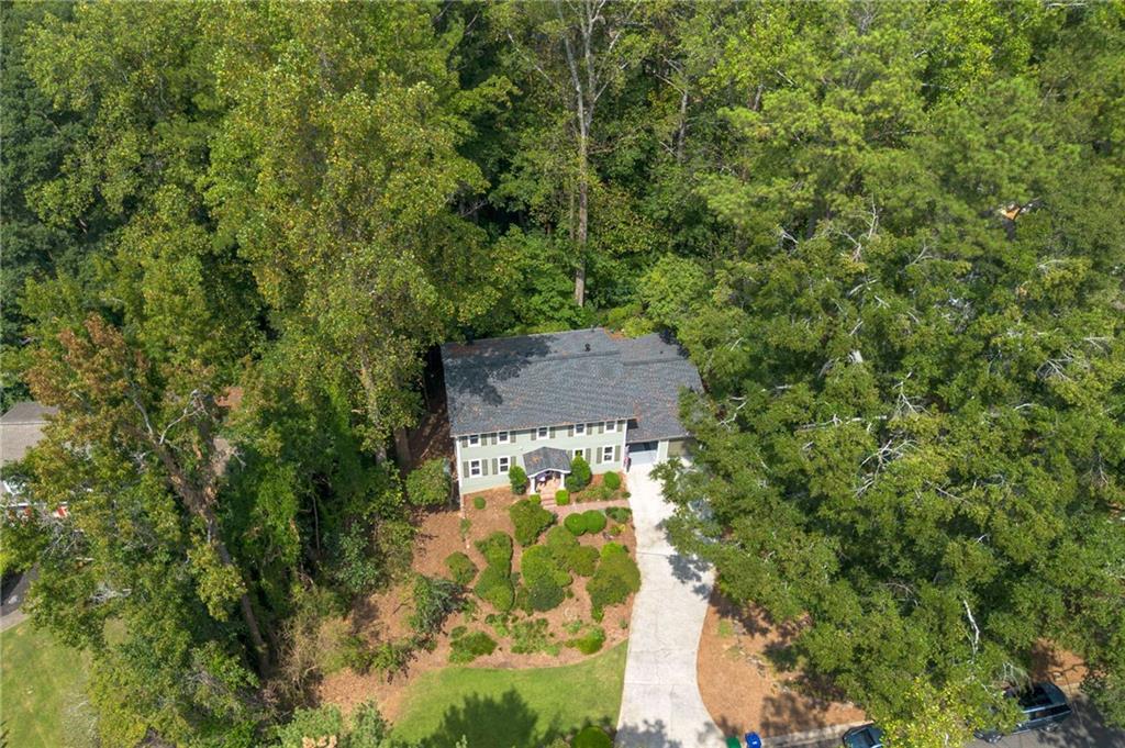 Aerial view of a two-story house surrounded by mature trees, landscaped gardens, and a curved driveway.