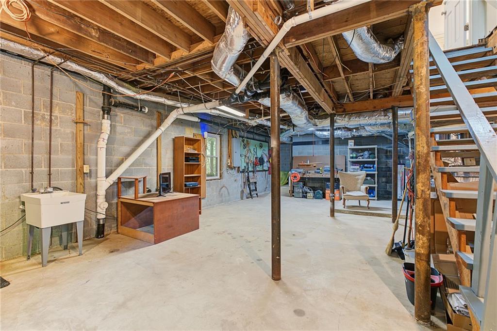 Unfinished basement with exposed joists, a concrete floor, utility sink, and staircase.