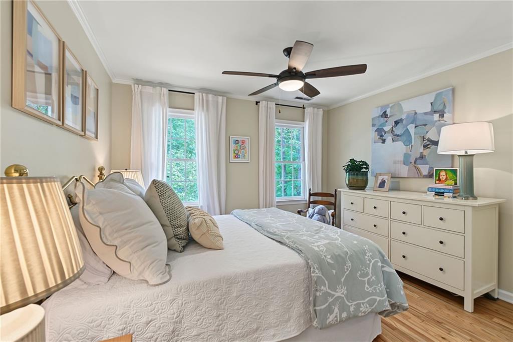 Bright bedroom with a white bed, two curtained windows, a dresser, and a ceiling fan.