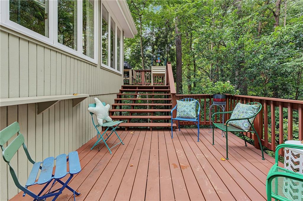 Wooden deck with colorful chairs, stairs, and a wooded backdrop.