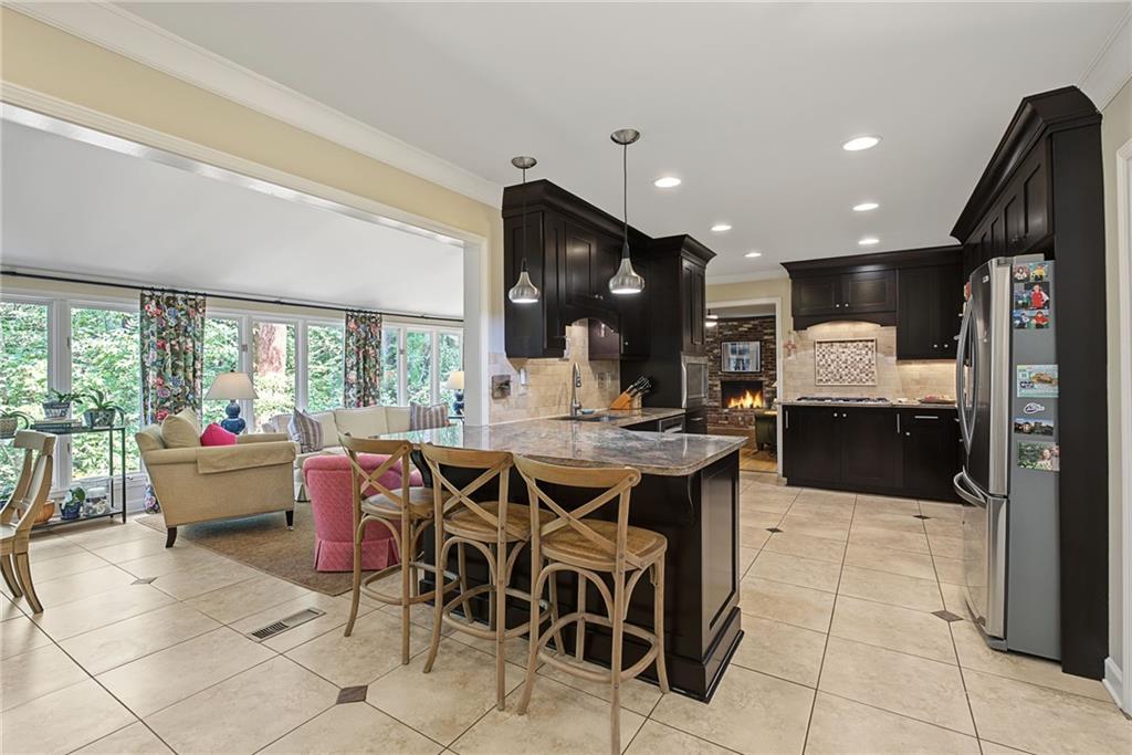 Kitchen with dark cabinetry, a granite island, bar seating, and an adjoining window-lined sitting area.