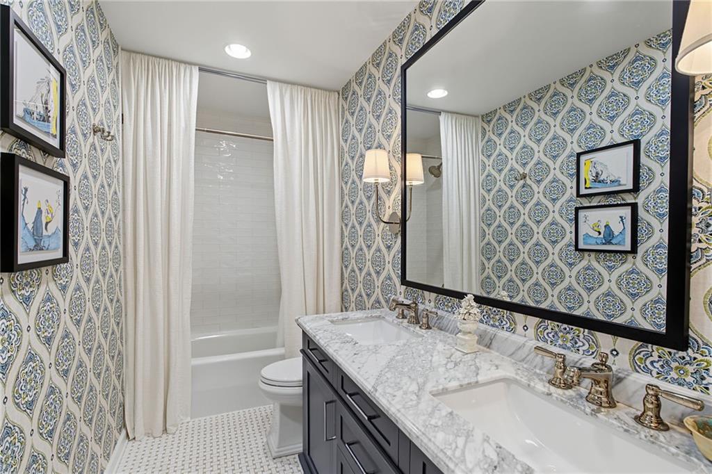 Bathroom with a marble double vanity, patterned wallpaper, and a curtained bathtub.