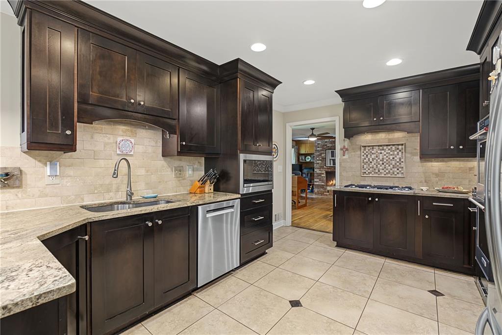 Kitchen with dark wood cabinetry, stone counters, stainless appliances, and a doorway to a living area.
