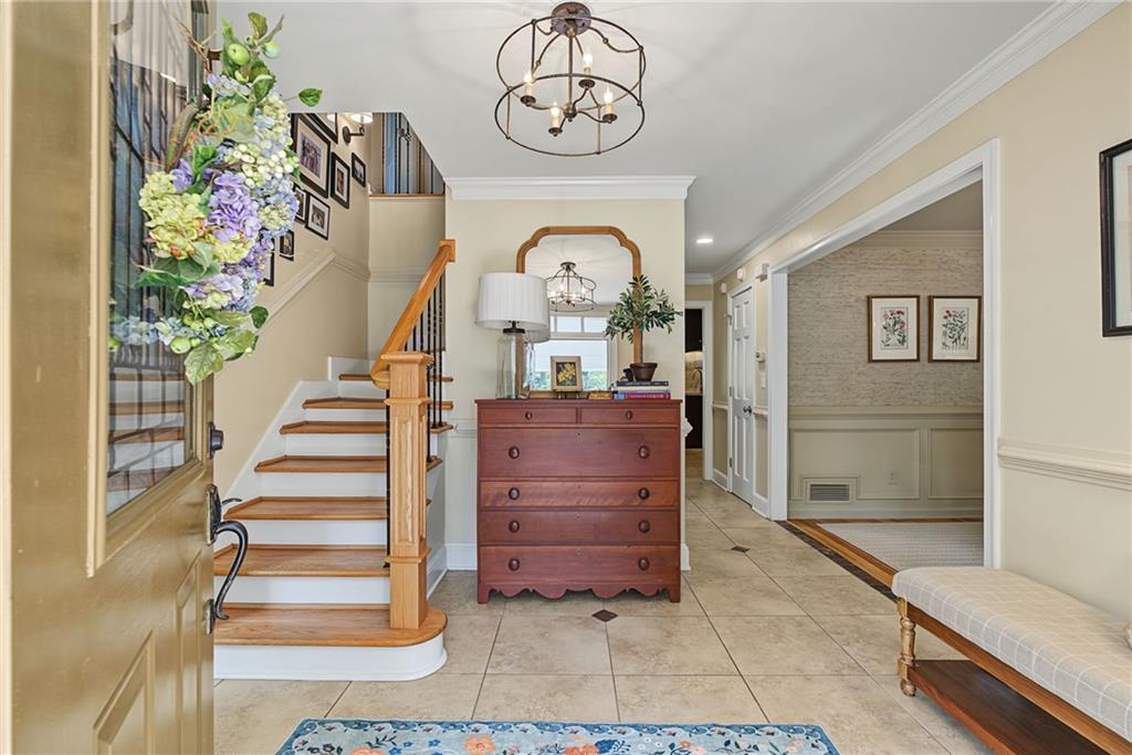 Foyer with a wood-and-white staircase, tiled floor, and dark chest beneath an arched mirror.