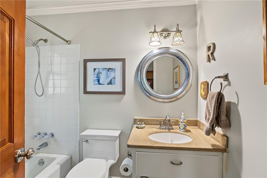 Bathroom with a tiled tub and shower beside a granite-topped vanity and large round mirror.
