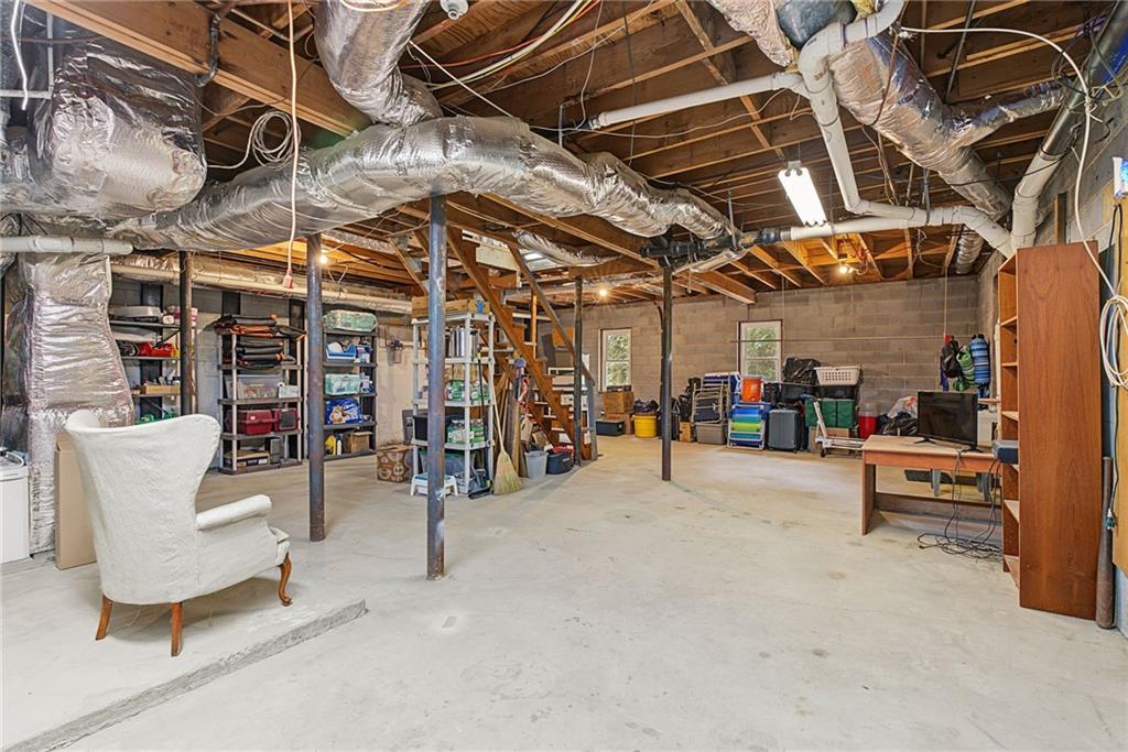 Basement with exposed ductwork, concrete floor, storage shelving, and a small work area.