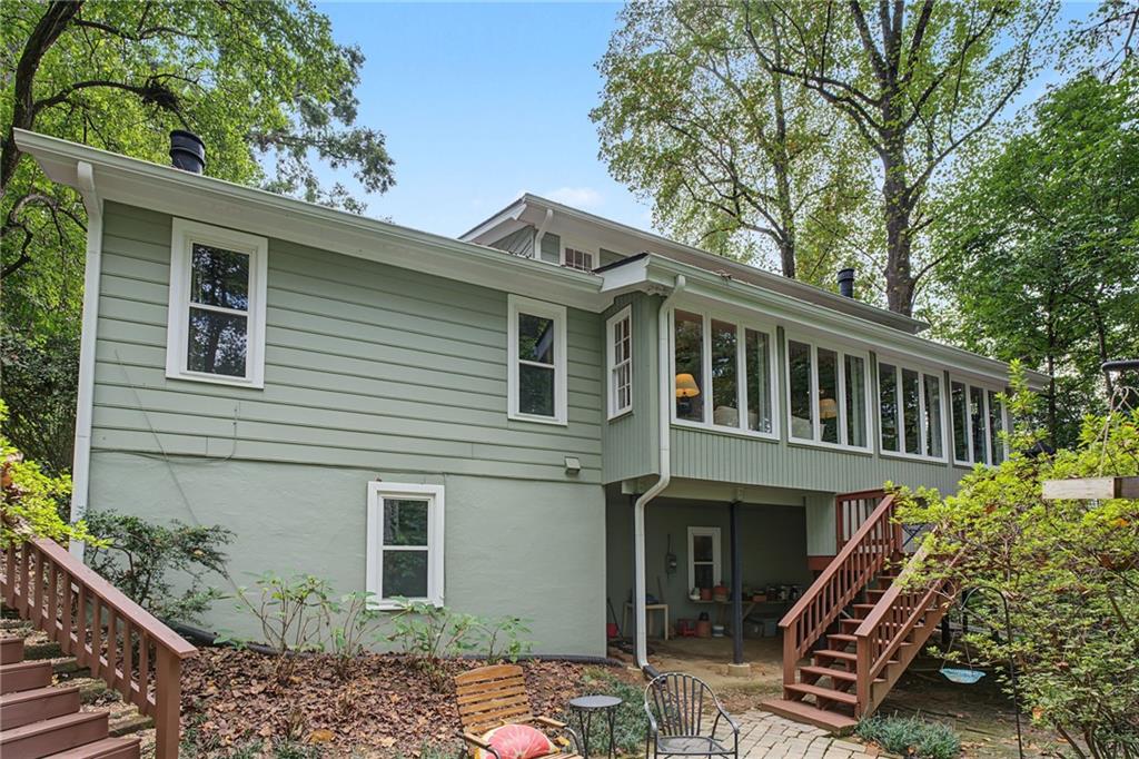 Rear of a light green split-level house with an enclosed sunroom and brick patio.