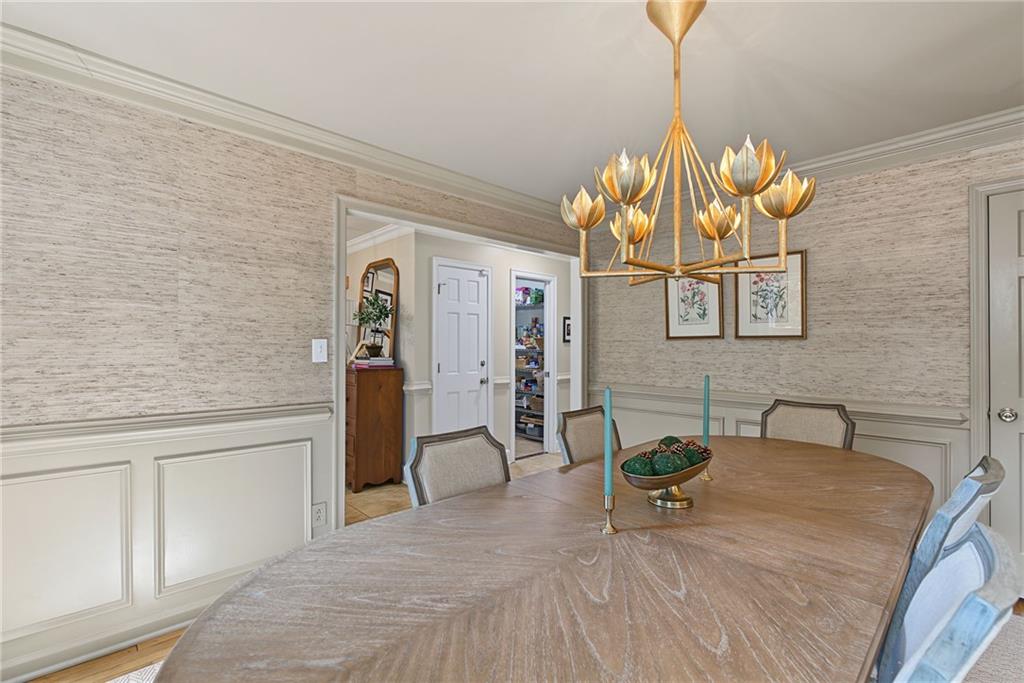 Dining room with an oval wood table, white wainscoting, textured wallpaper, and a gold chandelier.