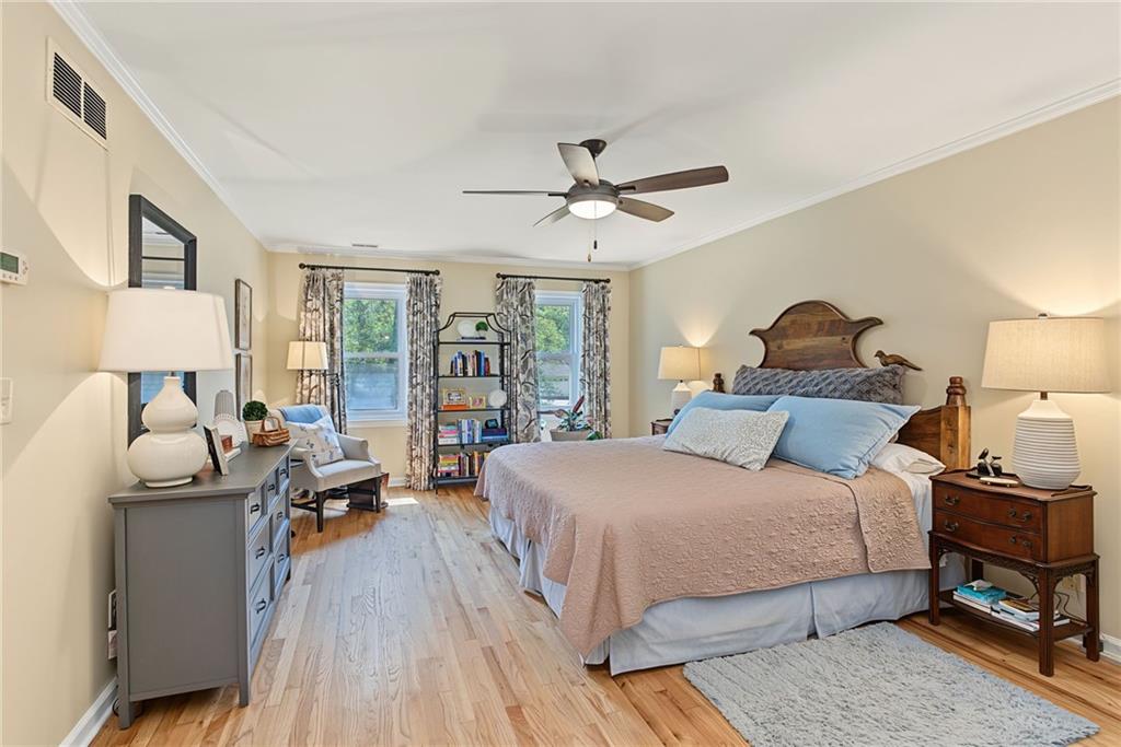 Bedroom with a large wooden bed, pale blue bedding, hardwood floors, and two curtained windows.