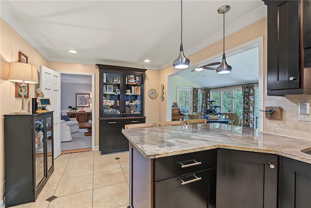 Kitchen with a large stone island and dark cabinetry, opening to a window-lined dining area.