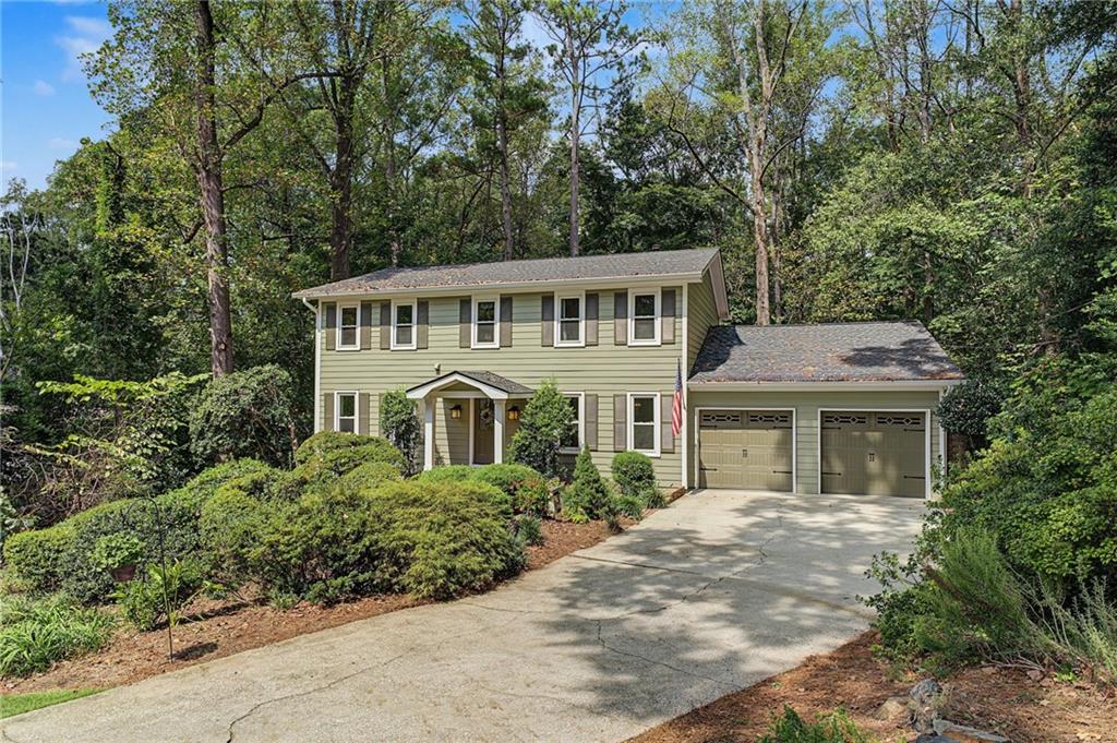 Pale green two-story house with an attached two-car garage and a tree-lined driveway.