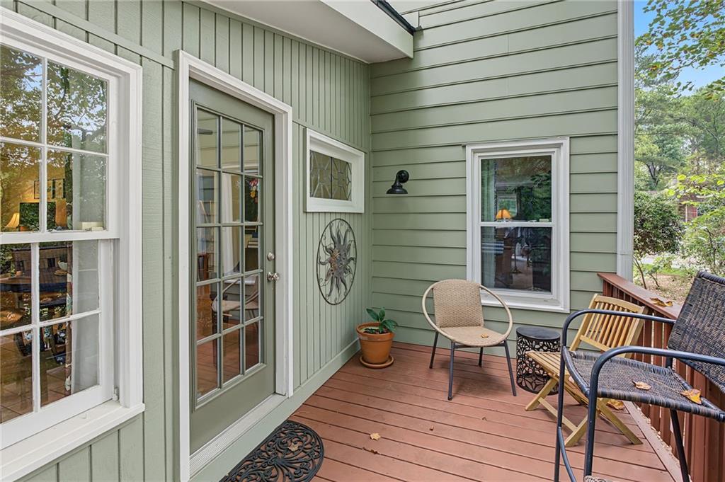 Covered porch with sage-green siding, glass-paneled door, and seating on a reddish-brown deck.