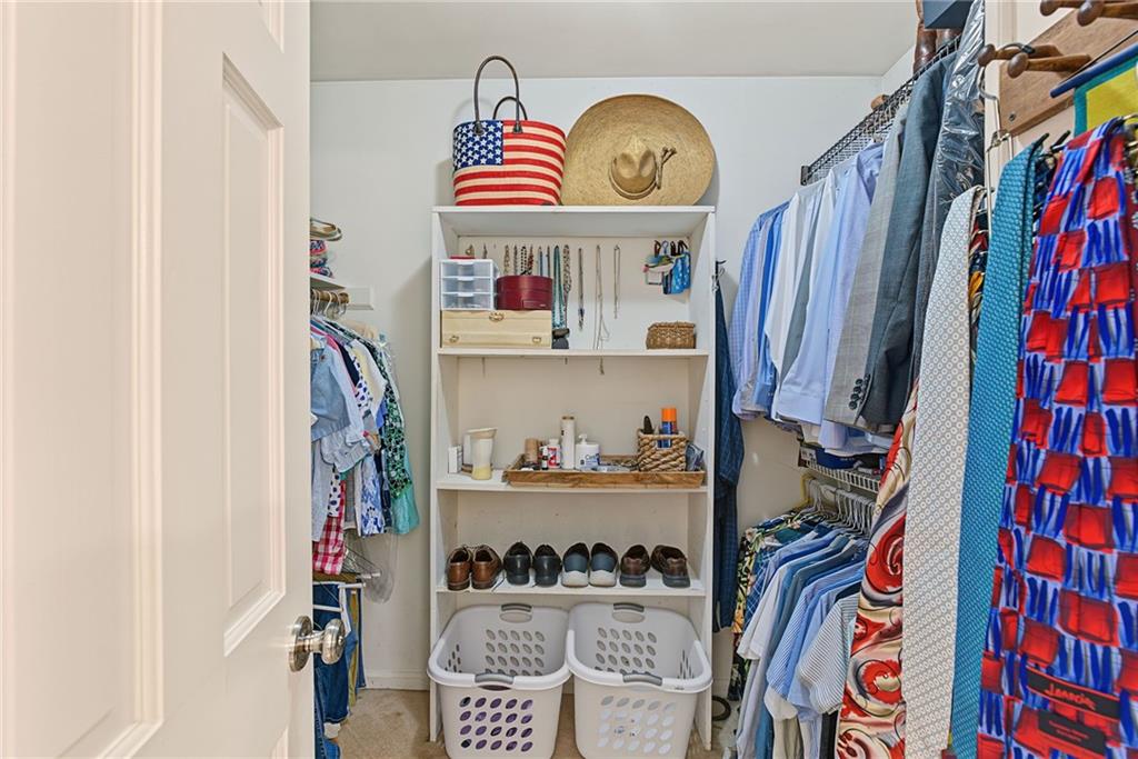 Walk-in closet with organized shelving, hanging clothes, shoes, and two laundry baskets.